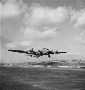 A world war two era fighter plane flies just above the runway on a cloudy day. 